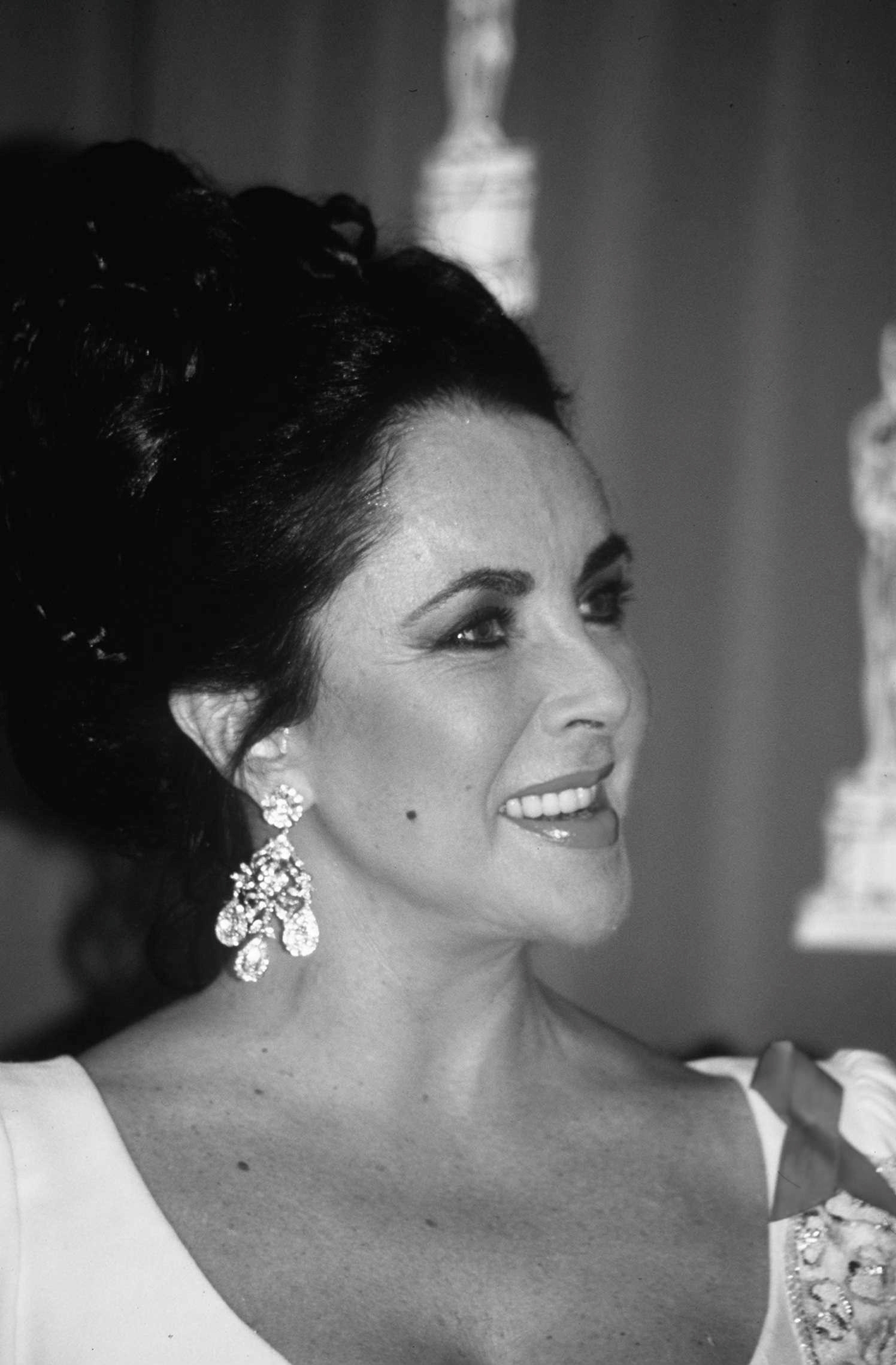 A dressed-up Elizabeth Taylor smiles and gazes to her left.