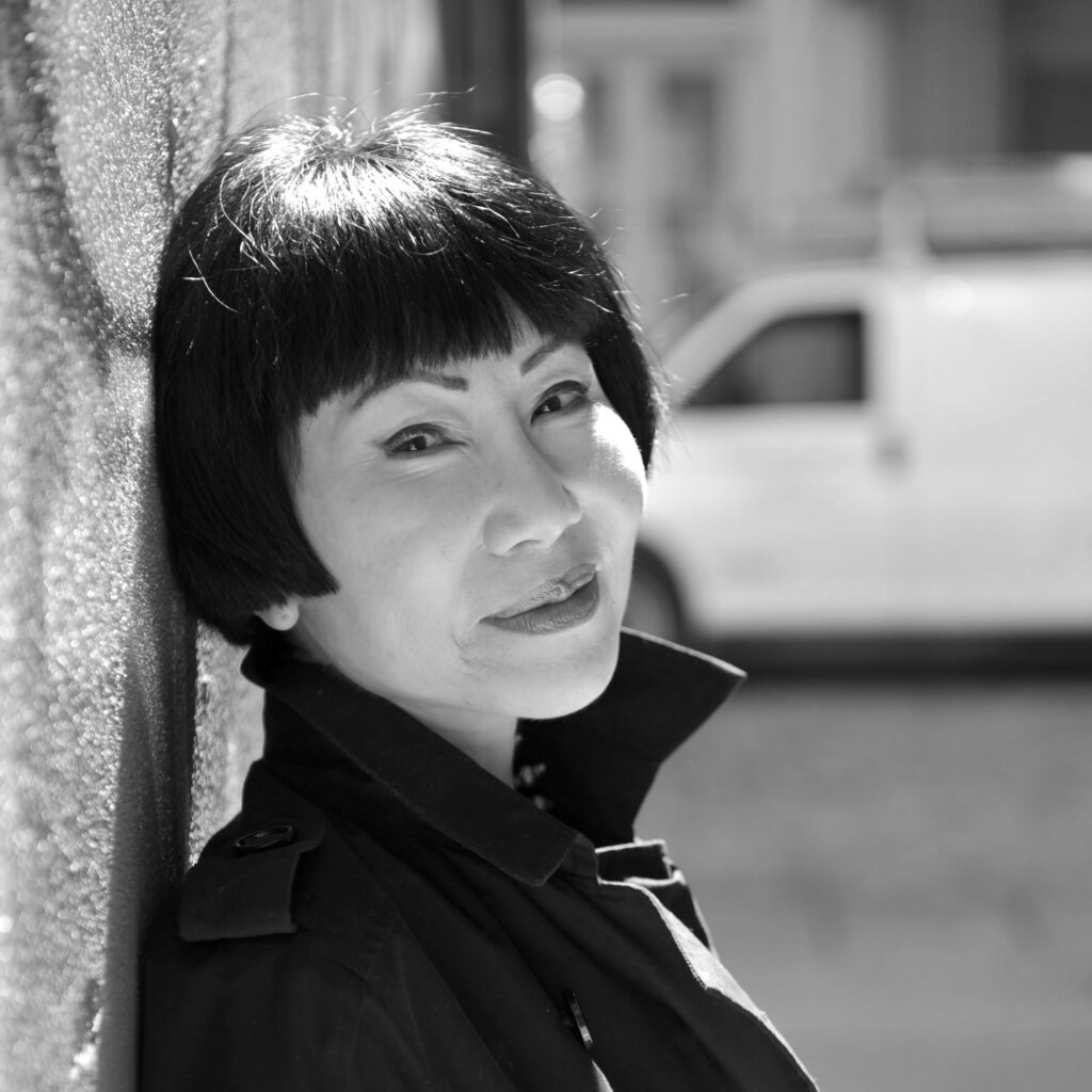 Headshot of Amy Tan leaning against a city wall.