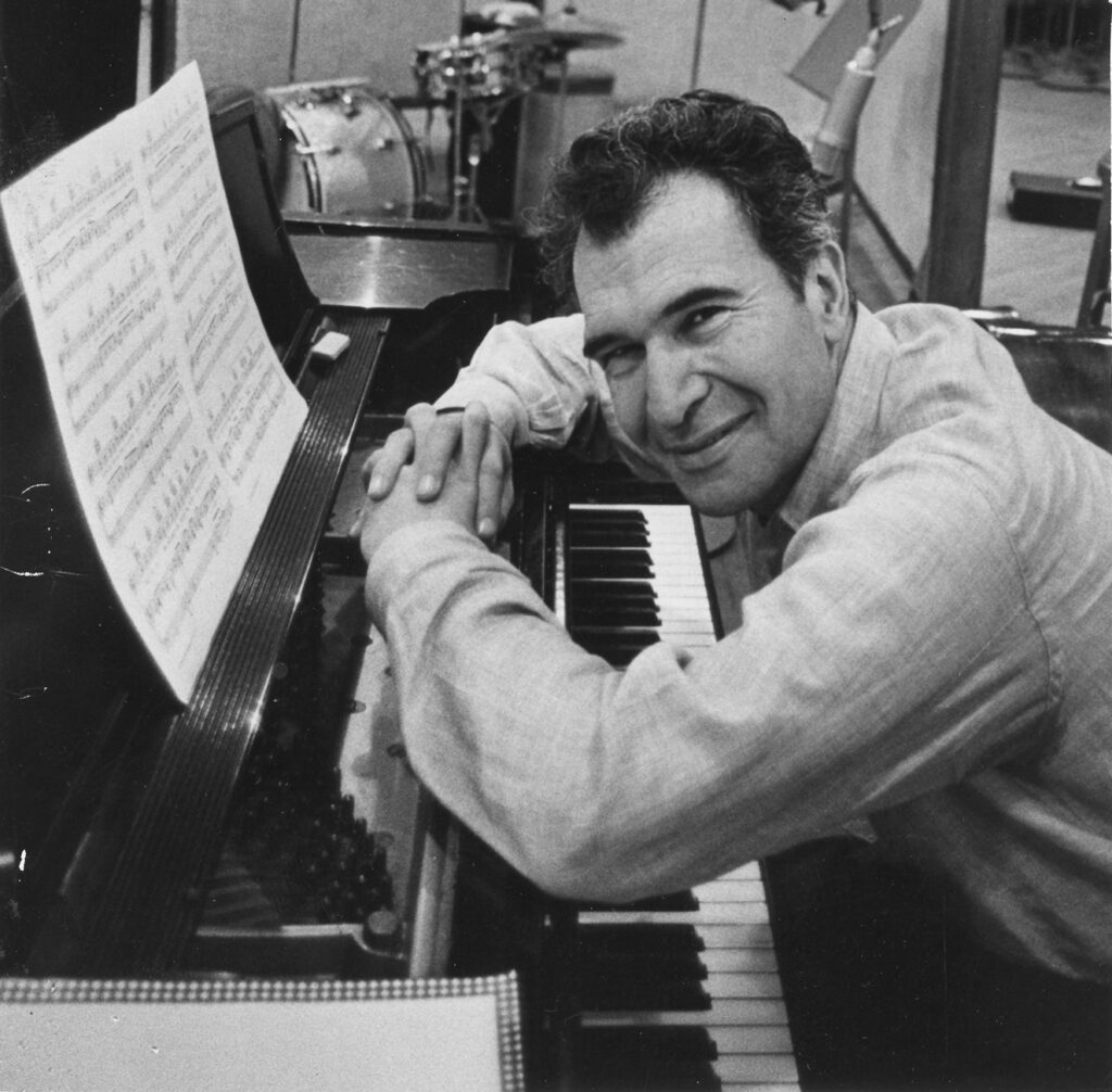 Dave Brubeck leans over a piano and smiles.