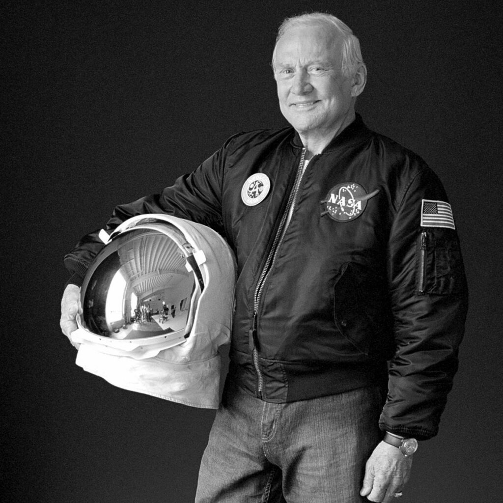 Buzz Aldrin poses with an astronaut helmet wearing a NASA jacket.