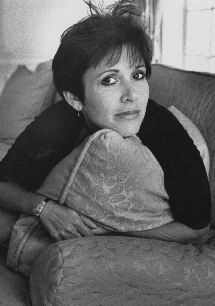 Carrie Fisher poses on a couch with a serious expression.