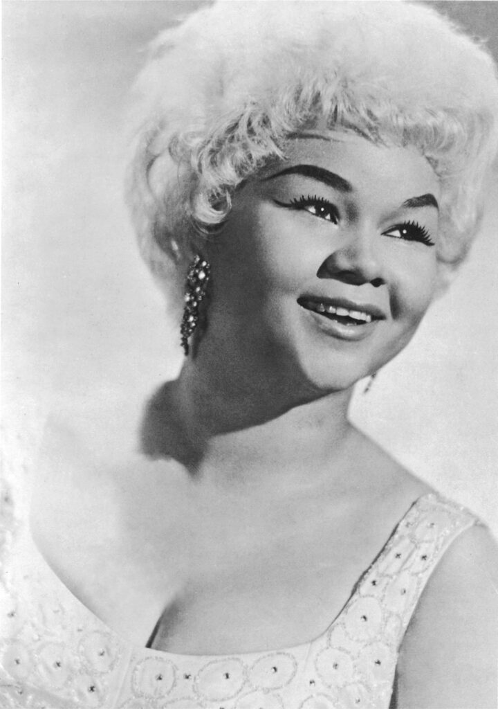 A young Etta James smiles while wearing performance attire.