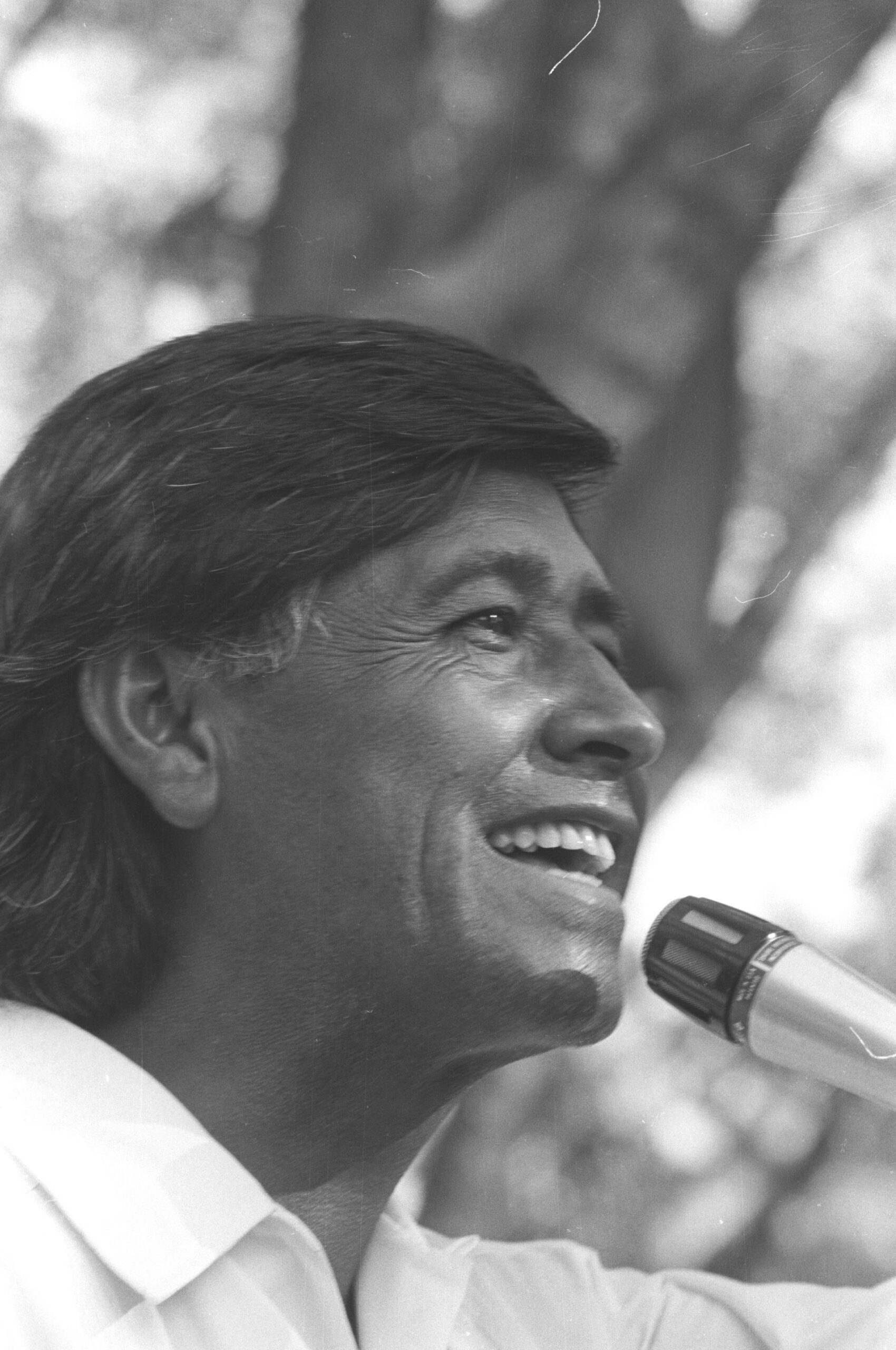 César Chávez speaks into a microphone with a smile.