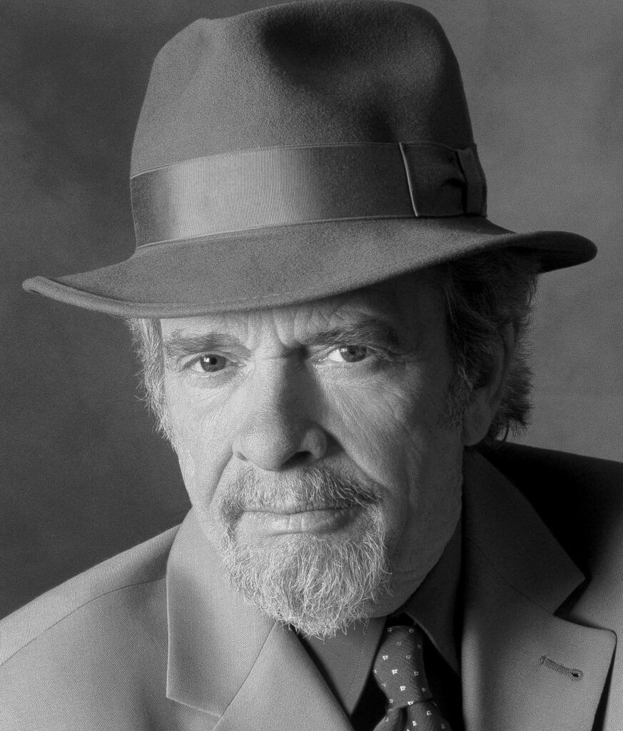 Headshot of a serious Merle Haggard in a brimmed hat and suit.