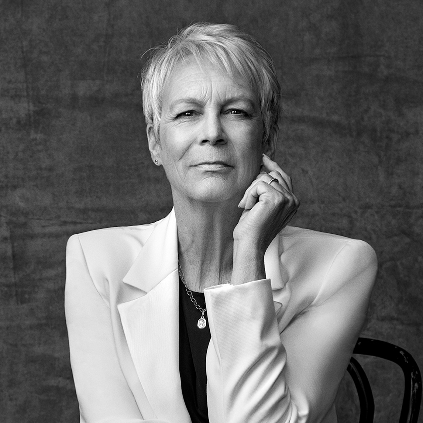 Jamie Lee Curtis sits in a chair with her hand on her face.