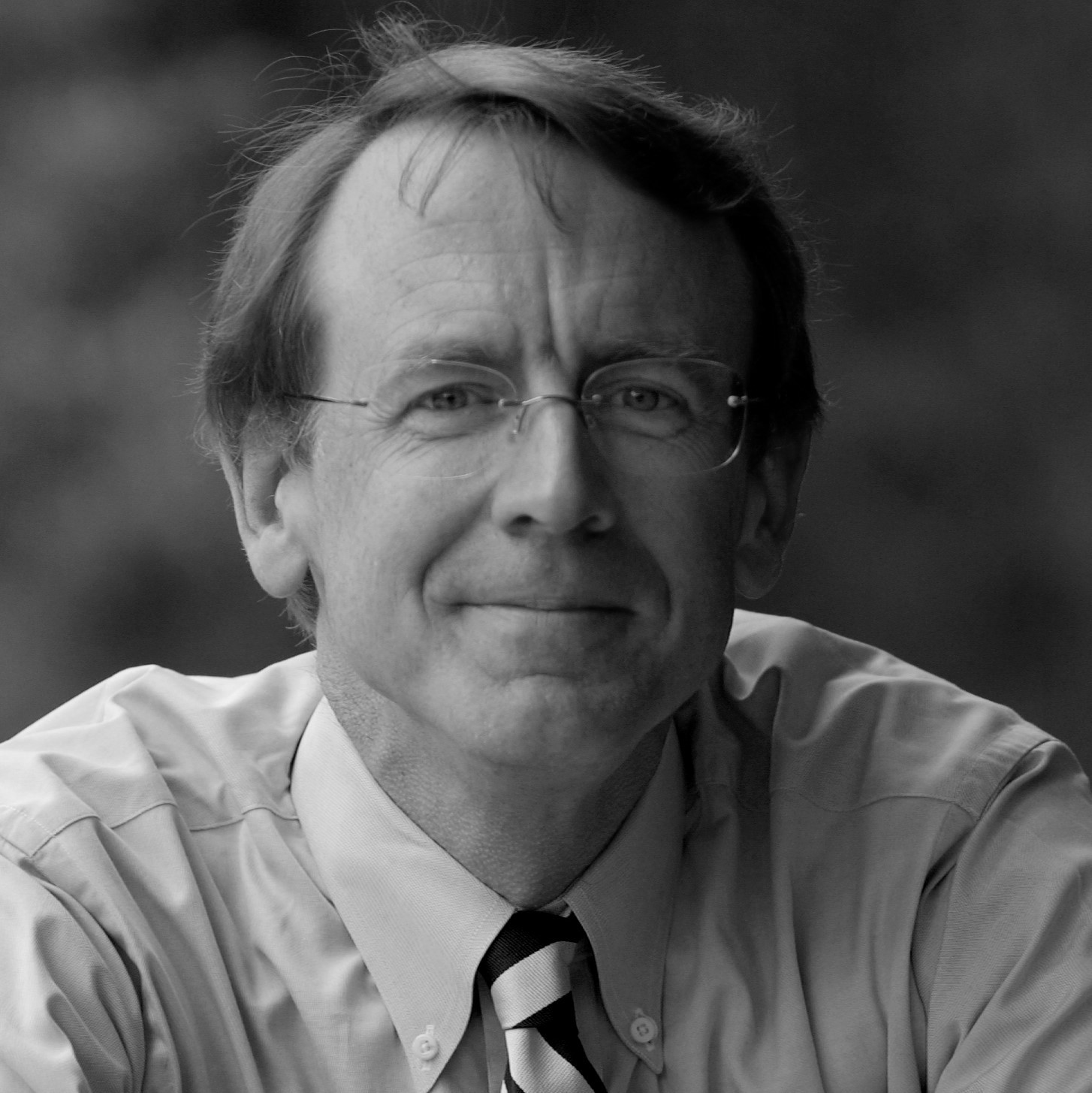 Headshot of a pleasantly smiling John Doerr in a button-up shirt and tie.