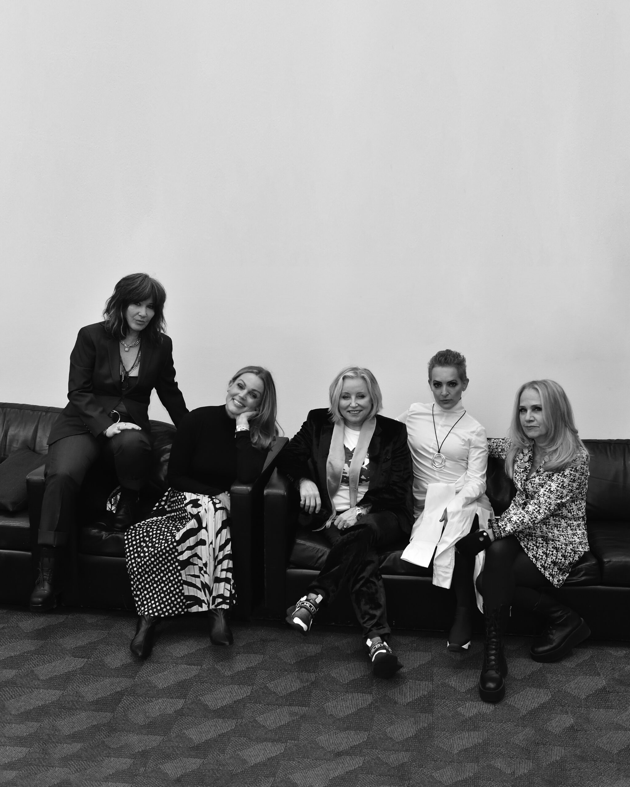 The Go-Go's pose with varied facial expressions while sitting on a couch.