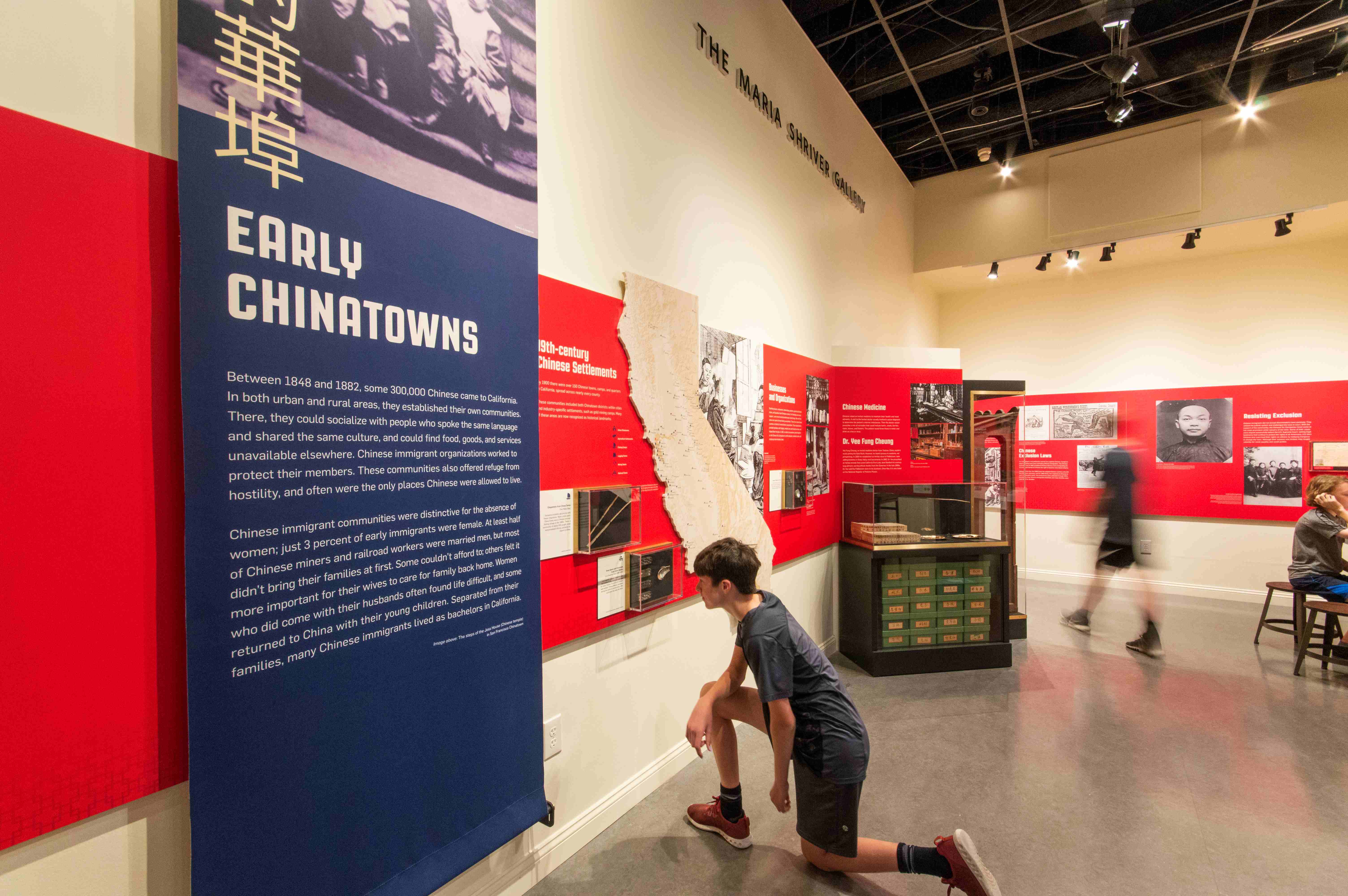 A boy kneeling down looking at an infographic in the Gold Mountain exhibit.