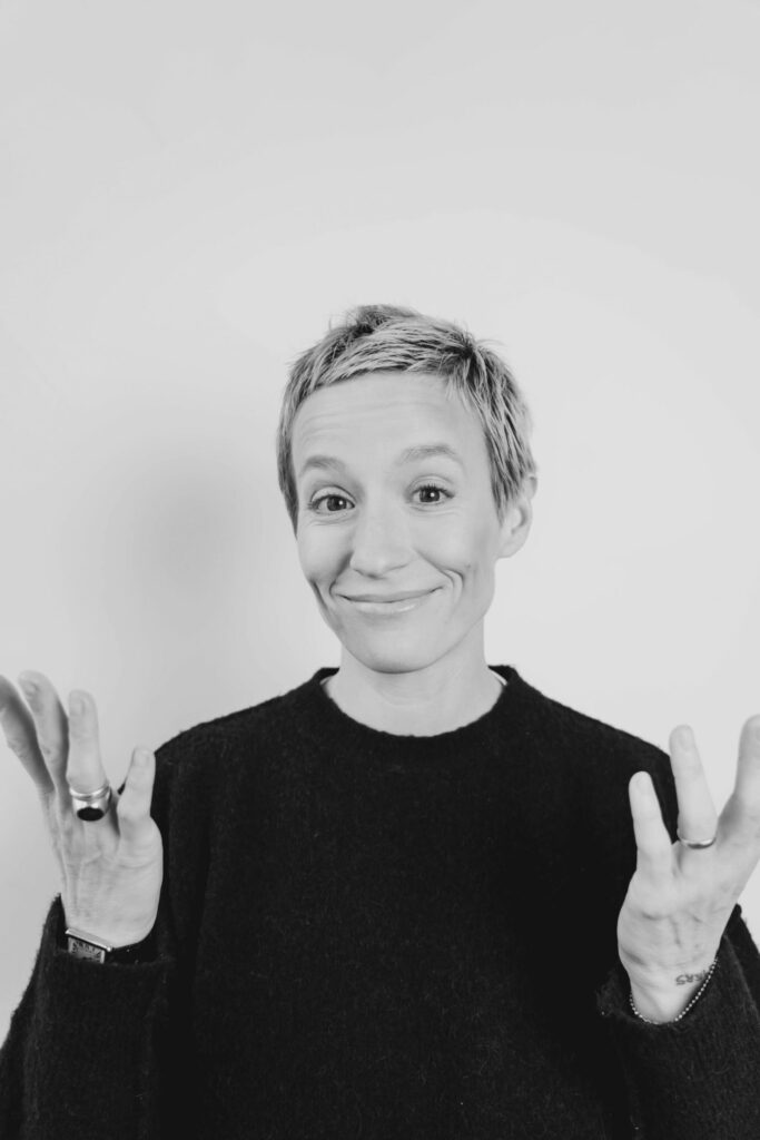 Headshot of Megan Rapinoe with arms lifted in subtle humor.