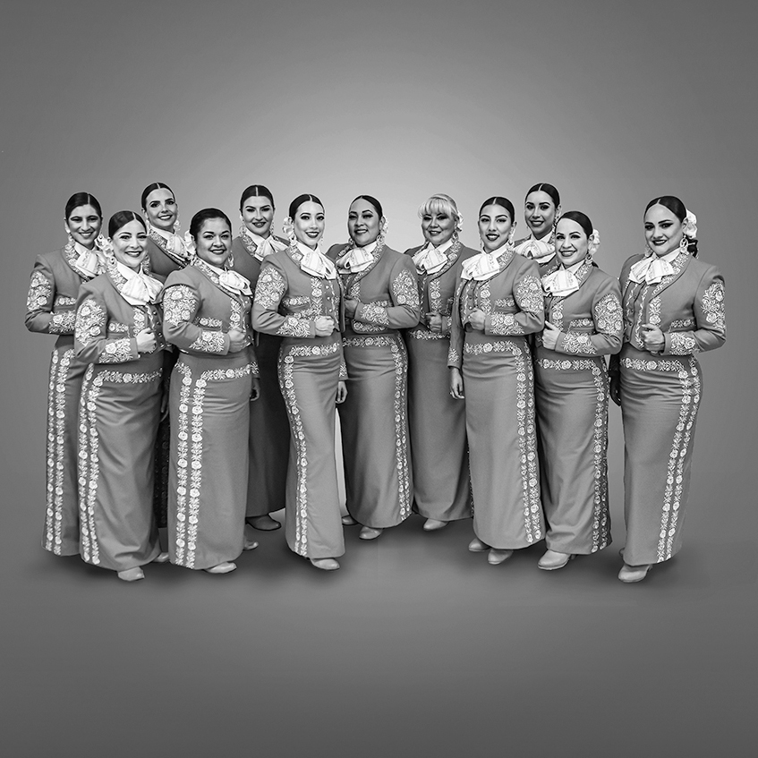 Mariachi Reyna de Los Ángeles all stand and smile at the camera, dressed alike.