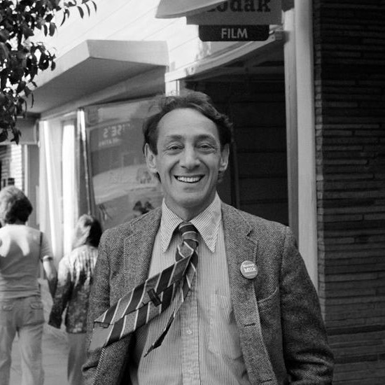 Harvey Milk smiles joyfully while his tie blows across his suit.