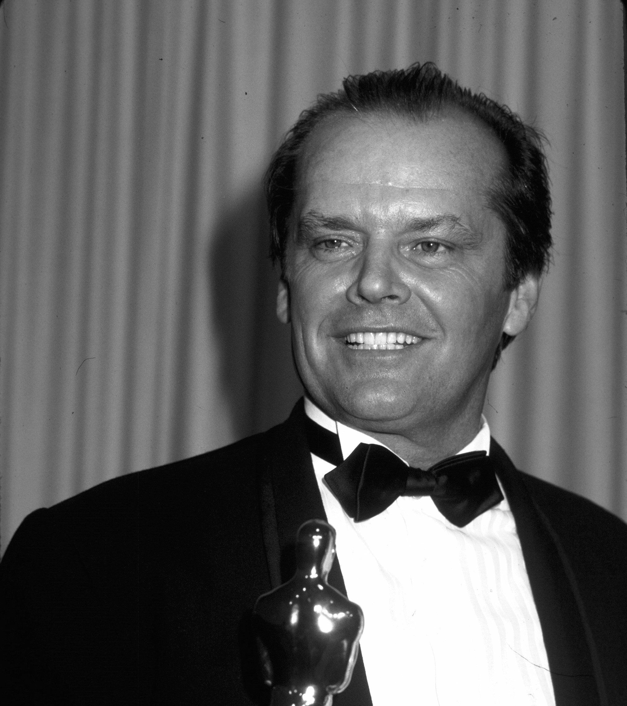 Jack Nicholson holds an Oscar and wears a tuxedo.