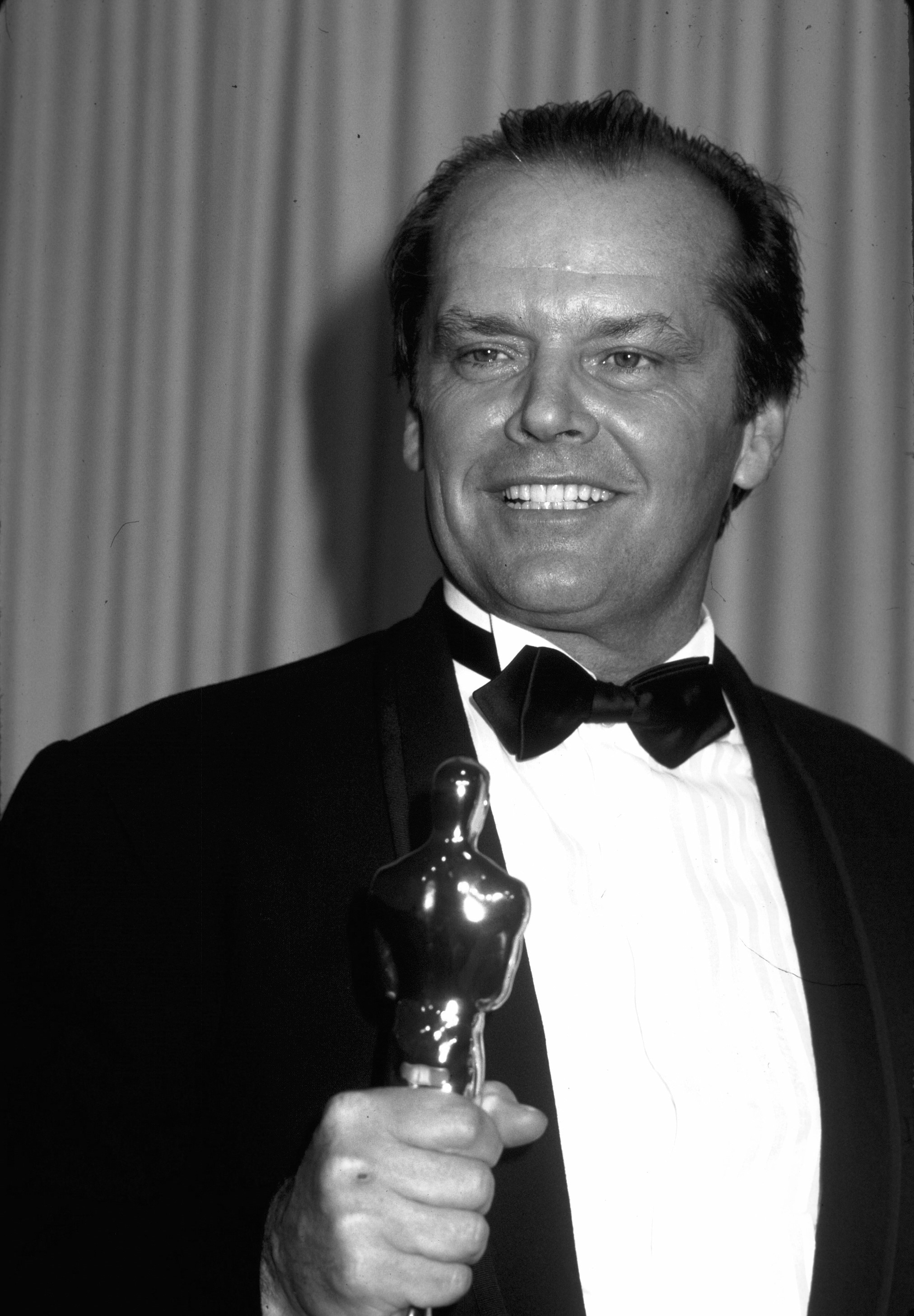 Jack Nicholson holds an Oscar and wears a tuxedo.