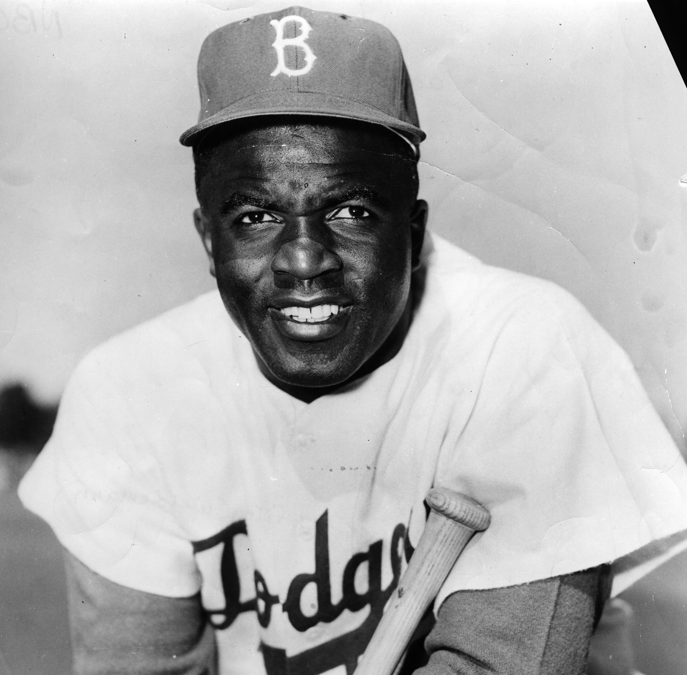 Jackie Robinson poses in his Dodgers uniform and holds a bat.