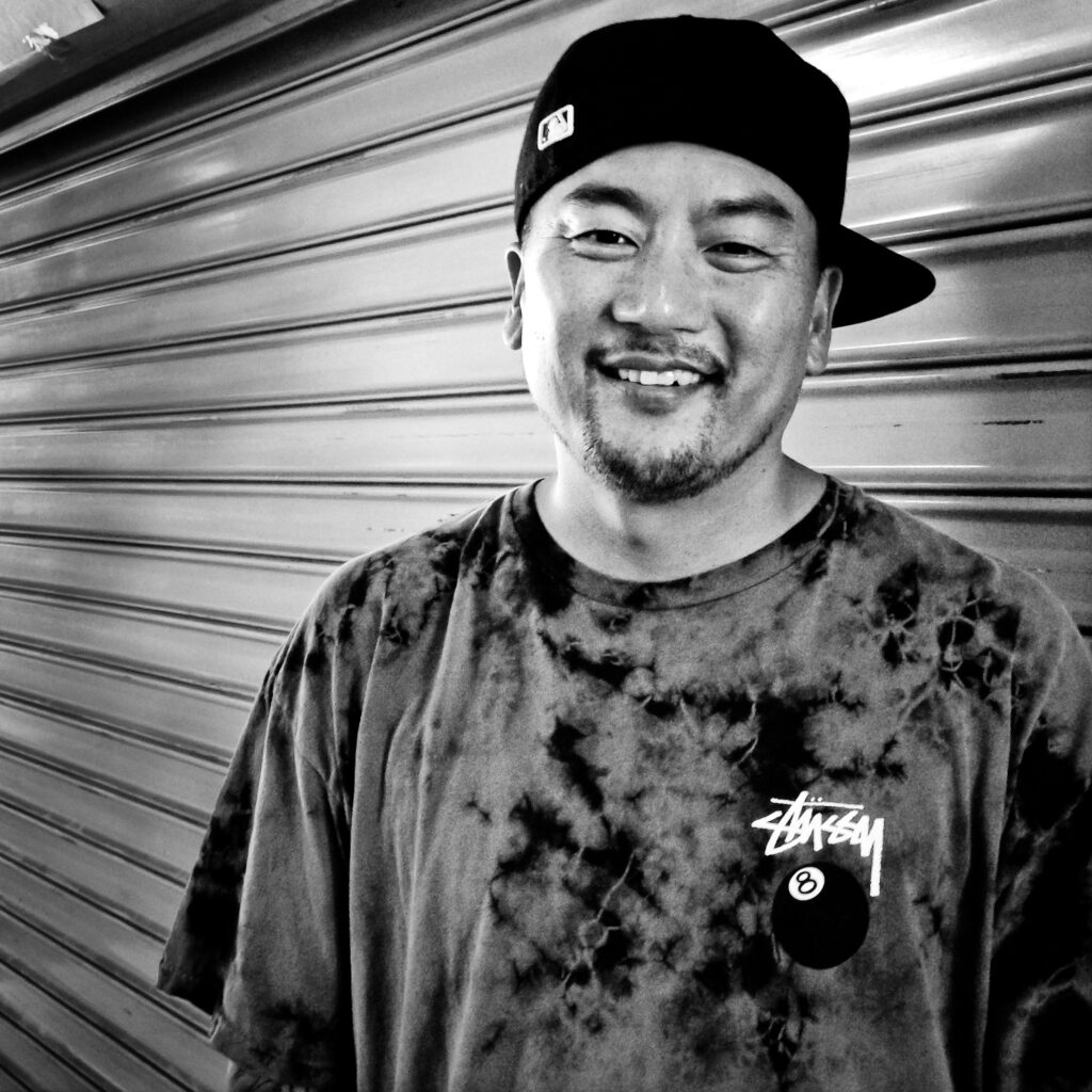 Headshot of Roy Choi wearing an 8 ball t-shirt and sideways baseball cap.