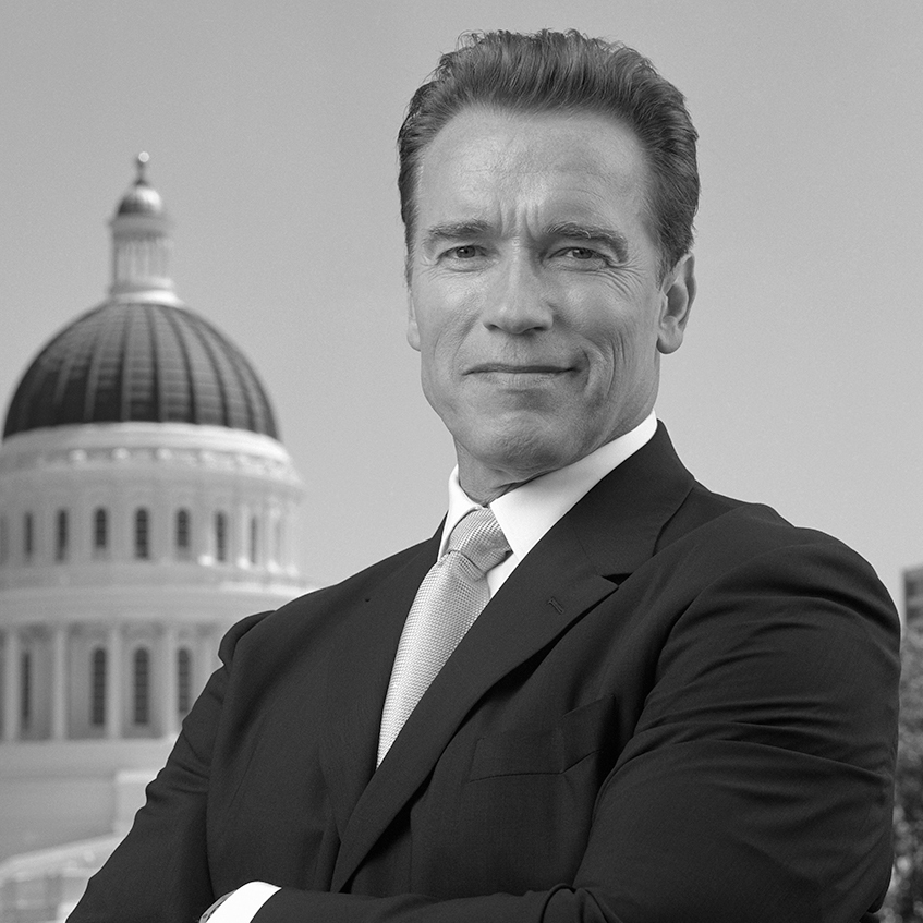Arnold Schwarzenegger stands in from of the California State Capitol with his arms crossed.