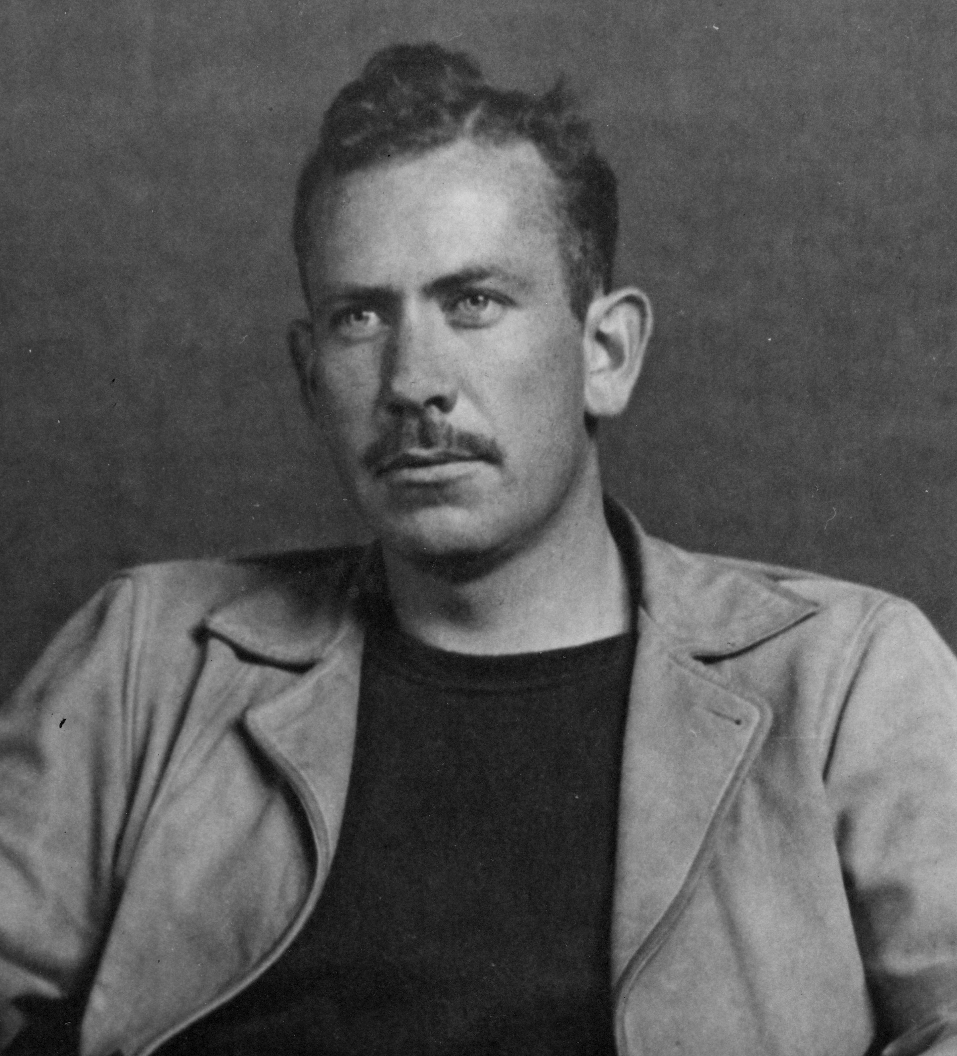 Headshot of a young John Steinbeck with a mustache and serious expression.
