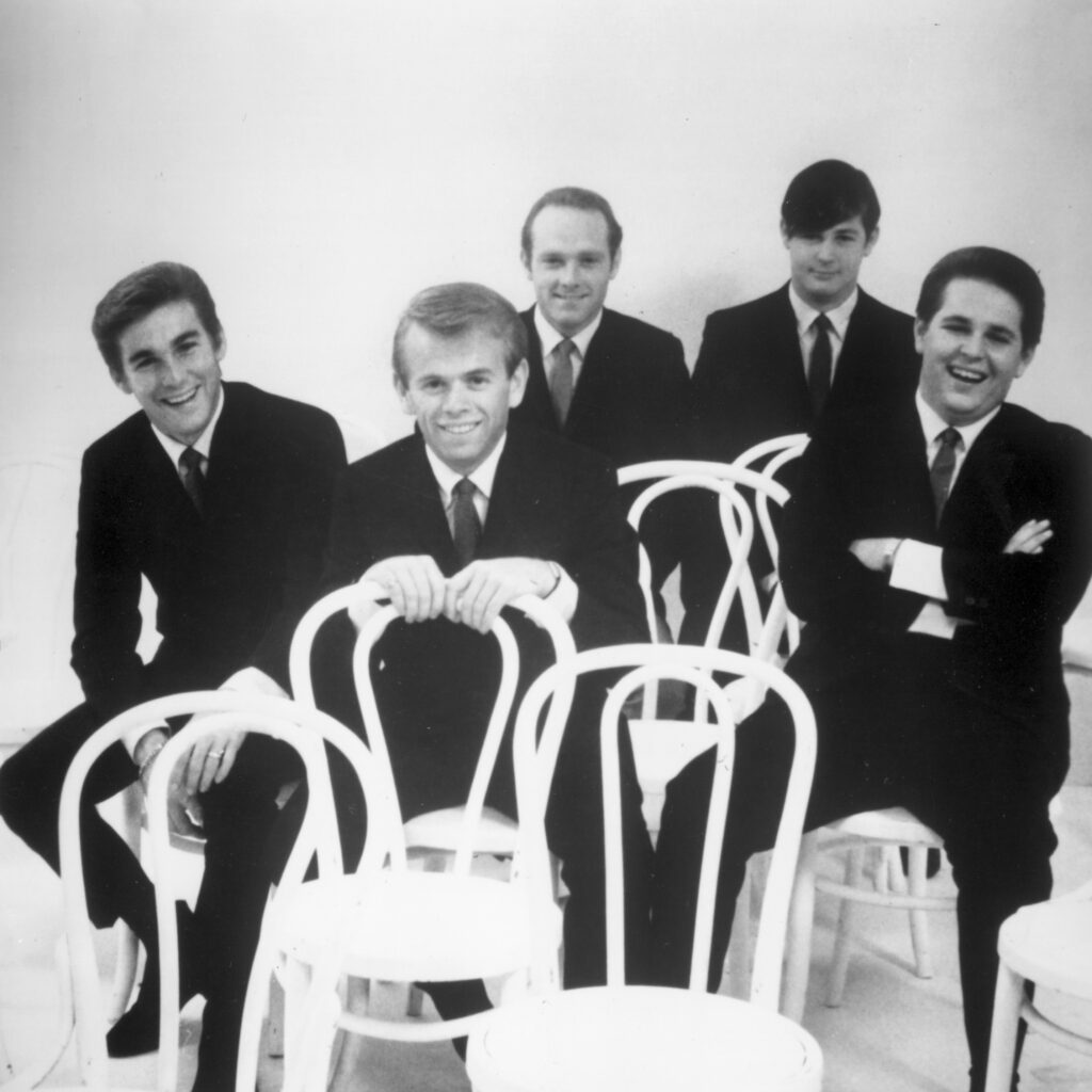 The Beach Boys sit on chairs in a staggered formation wearing matching suits and ties.