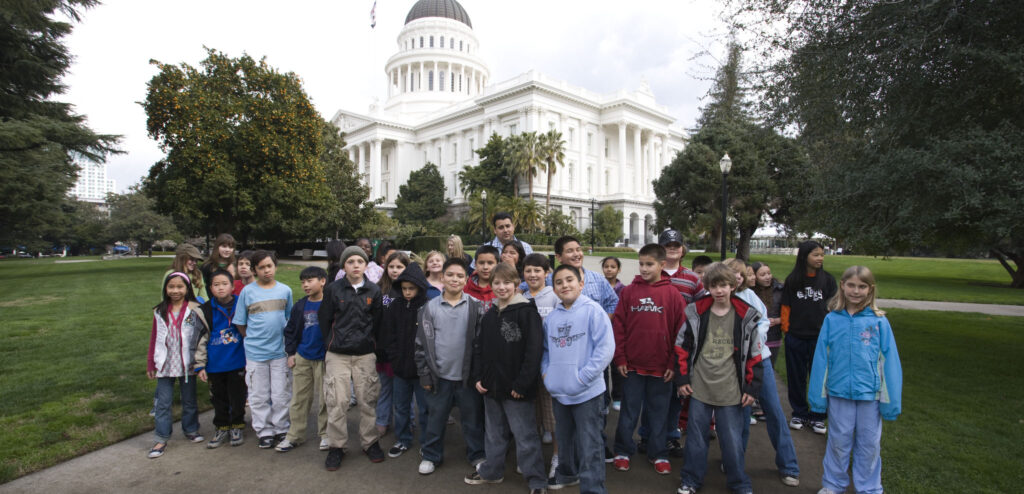 A group of students pose for a picture in Capitol Park with the California State Capitol in the background.