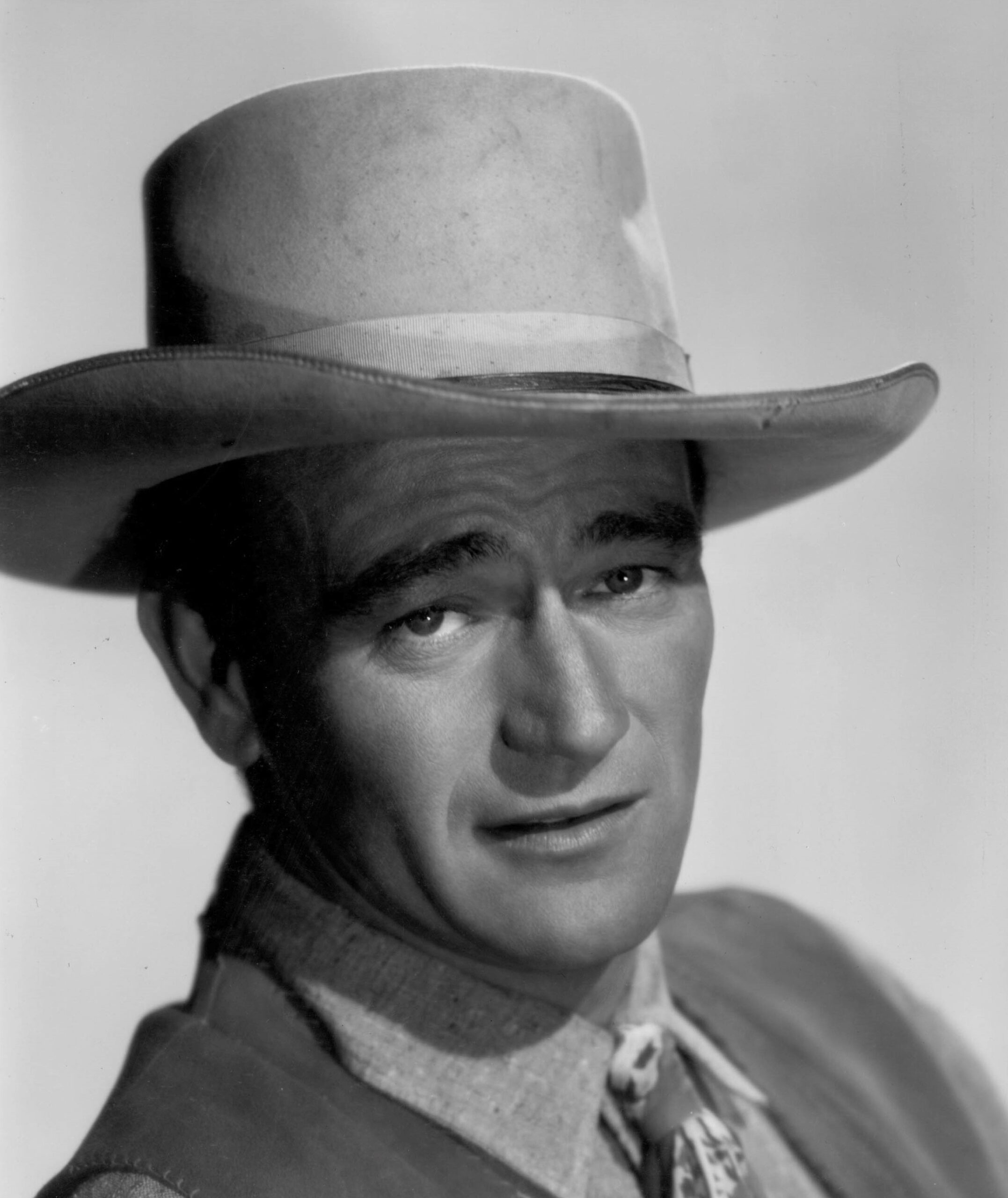 Headshot of John Wayne with eyebrows raised wearing a wide-brimmed hat.