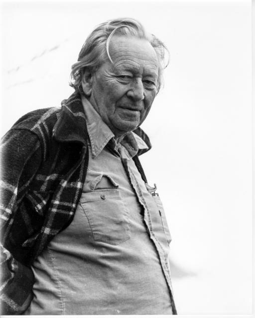 Gregory Bateson gazes downward wearing a casual button-up shirt and plaid jacket.