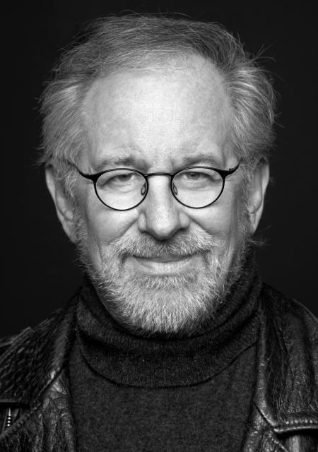 Headshot of Steven Spielberg wearing a turtle neck, leather jacket, and round glasses.