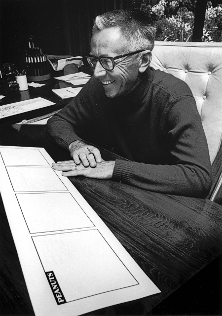 Charles Schulz faces a blank Peanuts comic strip and smiles joyously.
