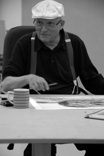 David Hockney sits behind an art work wearing a cap and suspenders.