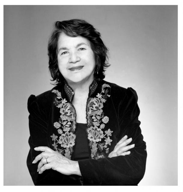 Headshot of Dolores Huerta posing warmly with arms crossed over an embroidered jacket.