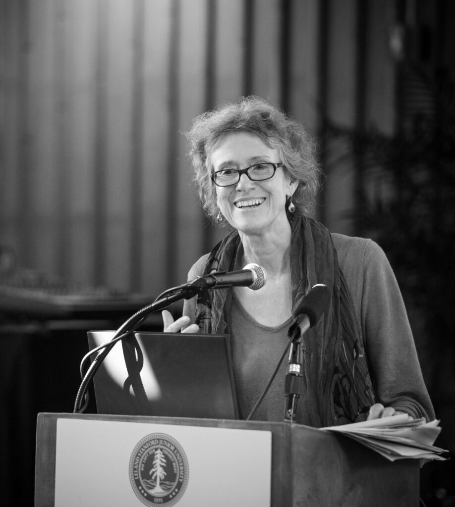 Arlie Hochschild smiles while speaking at a podium.