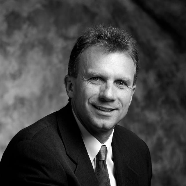 Headshot of Joe Montana smiling and wearing a suit and tie.