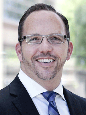 Headshot of Brad Pacheco in a suit, tie and glasses.