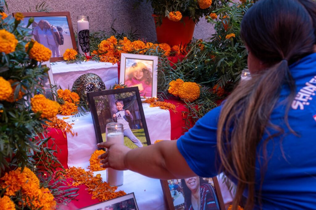 woman places a candle on an altar with photos and marigold decorations.