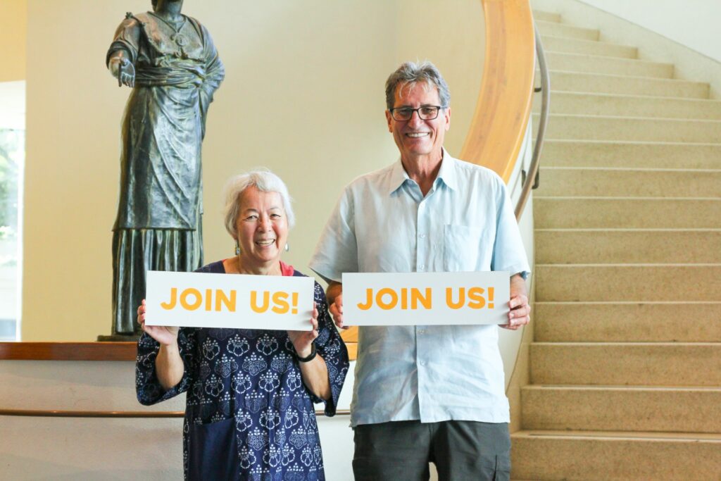 Two senior members hold signs reading "Join Us"