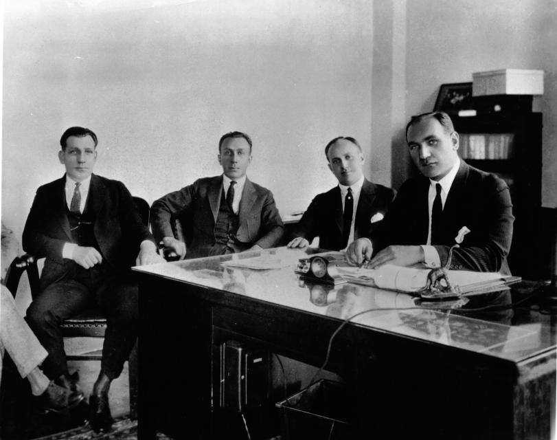 The Warner brothers pose seriously while sitting at a table.